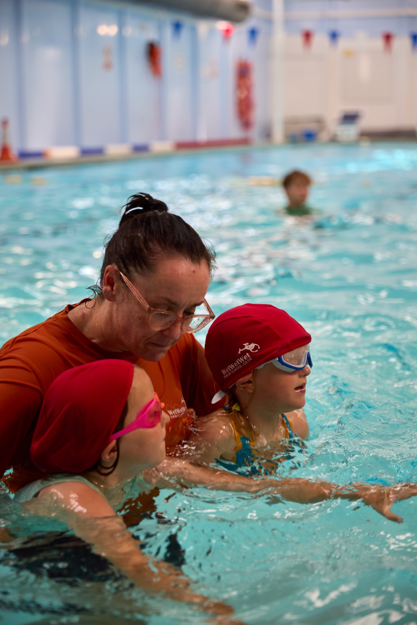 Instructor teaching two girls in red swim caps